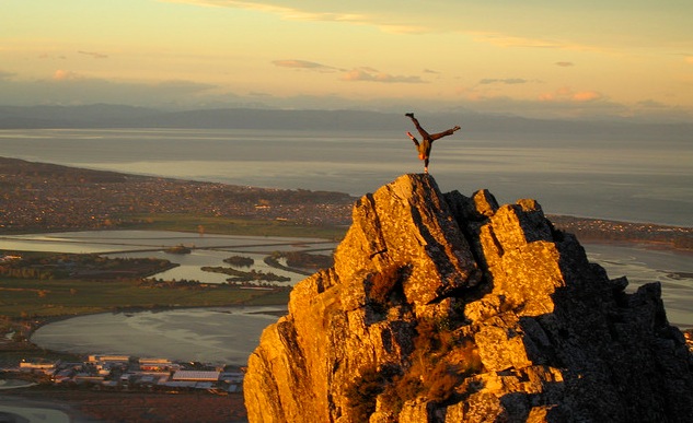 man does one-handed handstand on mountain